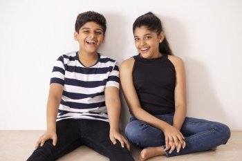 Cheerful boy and girl sitting together on floor against white wall