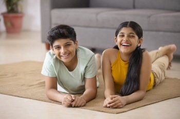 Portrait of cheerful boy and girl lying down on floor in living room