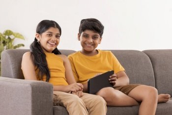 Boy and girl using digital tablet while sitting on sofa in living room