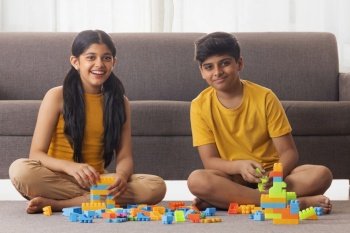 Boy and girl playing with toy blocks in living room at home