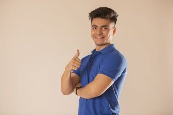 Young man in blue t-shirt showing thumbs up against white background