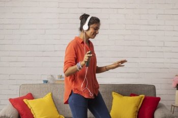 Cheerful woman listening music on headphones and dancing in living room