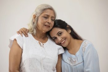 A YOUNG WOMAN LEANING ON HER MOTHER'S SHOULDER AND SMILING AT CAMERA