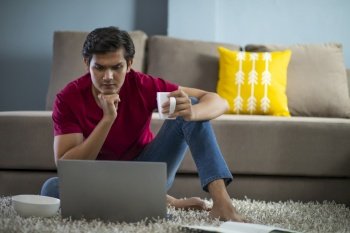 YOUNG COLLEGE STUDENT WITH A MUG IN HAND ATTENDING ONLINE CLASS 