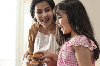 A HAPPY MOTHER GIVING CUPCAKES TO DAUGHTER
