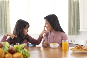 A DAUGHTER HAPPILY PLAYING WITH MOTHER WHILE HAVING BREAKFAST