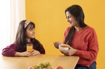 A MOTHER AND DAUGHTER HAPPILY LOOKING AT EACH OTHER WHILE HAVING BREAKFAST
