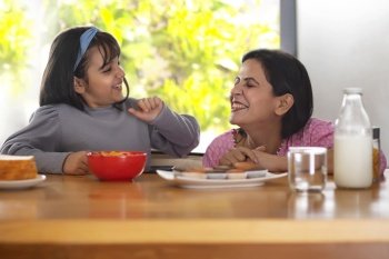 A YOUNG DAUGHTER AND MOTHER PLAYFULLY SITTING WITH EACH OTHER WHILE EATING FOOD