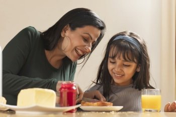 A MOTHER HAPPILY SPREADING JAM ON BREAD FOR DAUGHTER
