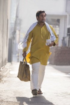 A RURAL MAN HOLDING BAG IN HAND WALKING ON A SUNNY DAY