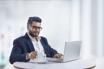 Young man sitting in his office while working on the laptop while drinking coffee. 