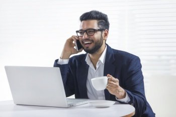 Young man talking on the phone while working on laptop in his office 