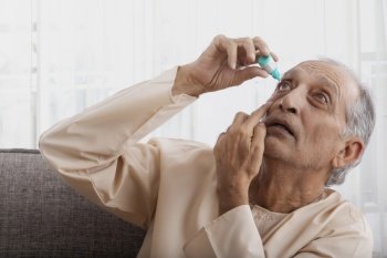 Senior man putting eye drops on his own. (Health and fitness) 