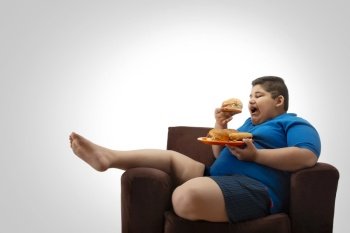 Young boy sitting on the sofa at home with a plate full of burgers. (Obesity) 