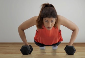 Woman doing pushups with dumbbells on a wooden floor. 