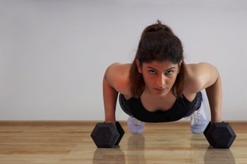 Woman doing pushups with dumbbells on a wooden floor. 