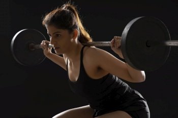 Woman working out with barbell in front of a dark background. 