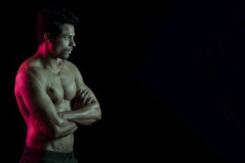 Man flexing his muscles in front of a dark background. 