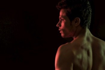 Bare chested man standing in front of a dark background. 