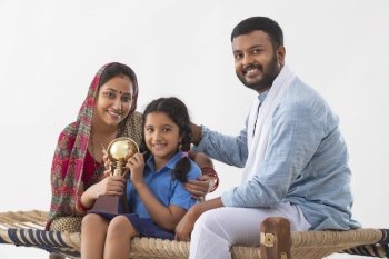 PORTRAIT OF A SMALL RURAL GIRL HAPPILY POSING WITH A TROPHY ALONG WITH PARENTS