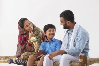 PORTRAIT OF A RURAL BOY SHOWING HAPPILY HIS TROPHY TO PARENTS