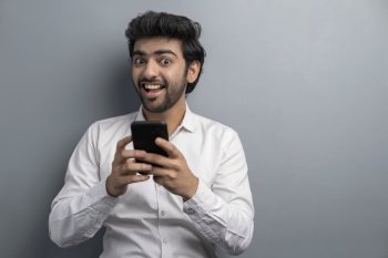 A YOUNG EXECUTIVE HAPPILY LOOKING AT CAMERA WHILE USING MOBILE PHONE