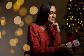 Young smiling woman in sweater holding a gift box celebrating winter holidays