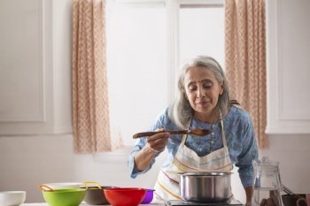 An old woman enjoying the aroma of the food she is cooking.
