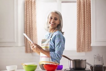 An old woman smiling in kitchen while holding a laptop with the recipe.