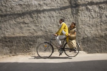A HAPPY HUSBAND RIDING BICYCLE WITH WIFE SITTING BEHIND