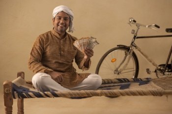 A TURBANED RURAL MAN HAPPILY HOLDING MONEY AND POSING IN FRONT OF CAMERA