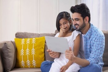 A FATHER AND DAUGHTER SITTING TOGETHER AND ENJOYING USING DIGITAL TABLET