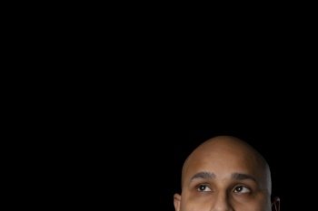 The shaved head and eyes of a bald man looking up against black background.