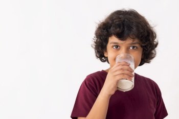 A YOUNG BOY DRINKING A GLASS OF MILK WHILE LOOKING AT CAMERA