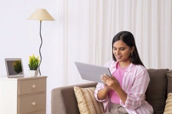 Indian girl looking at her tablet while sitting on sofa