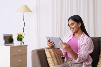 Indian girl watching her tablet while sitting on sofa