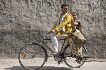 A HUSBAND RIDING A BICYCLE WITH WIFE SITTING BEHIND