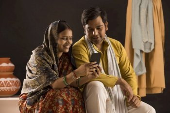A RURAL WIFE AND HUSBAND SITTING TOGETHER AND USING MOBILE PHONE