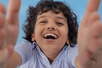 A BOY LAUGHING WHILE RAISING HANDS AND LOOKING AT CAMERA