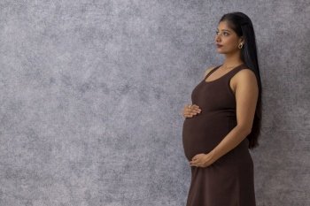 Pregnant woman standing against wall with holding her stomach