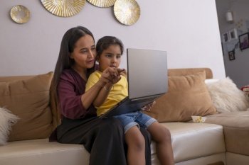 Mother and daughter playing video game on laptop on sofa in living room