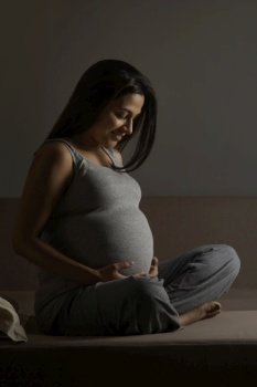 Pregnant woman sitting on the bed and holding her baby bump. 