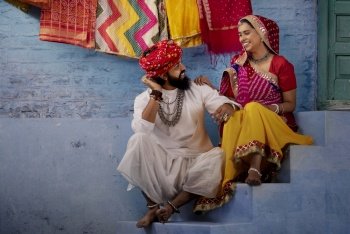 Rajasthani couple sitting on stairs sharing a light moment, as the husband plays ektara