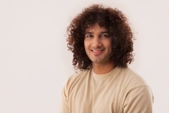 A YOUNG MAN WITH CURLY HAIR LOOKING AT CAMERA AND SMILING