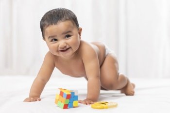 Cute baby in diaper playing with toys on bed