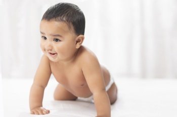 Cute baby in diaper crawling on bed