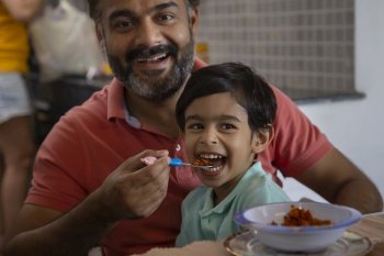Close-up portrait of caring father feeding his son with spoon