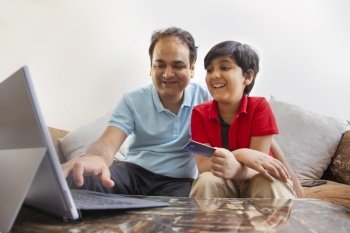 Father and son together shopping online through laptop using credit card