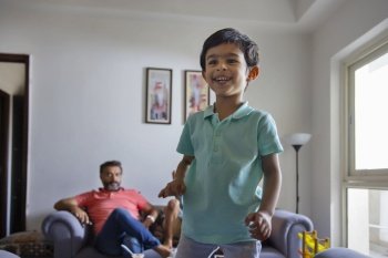 Cute child looking away with smile and the rest of his family sitting on sofa away