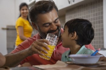 Close-up portrait of caring father feeding orange juice to his little child and mother standing behind